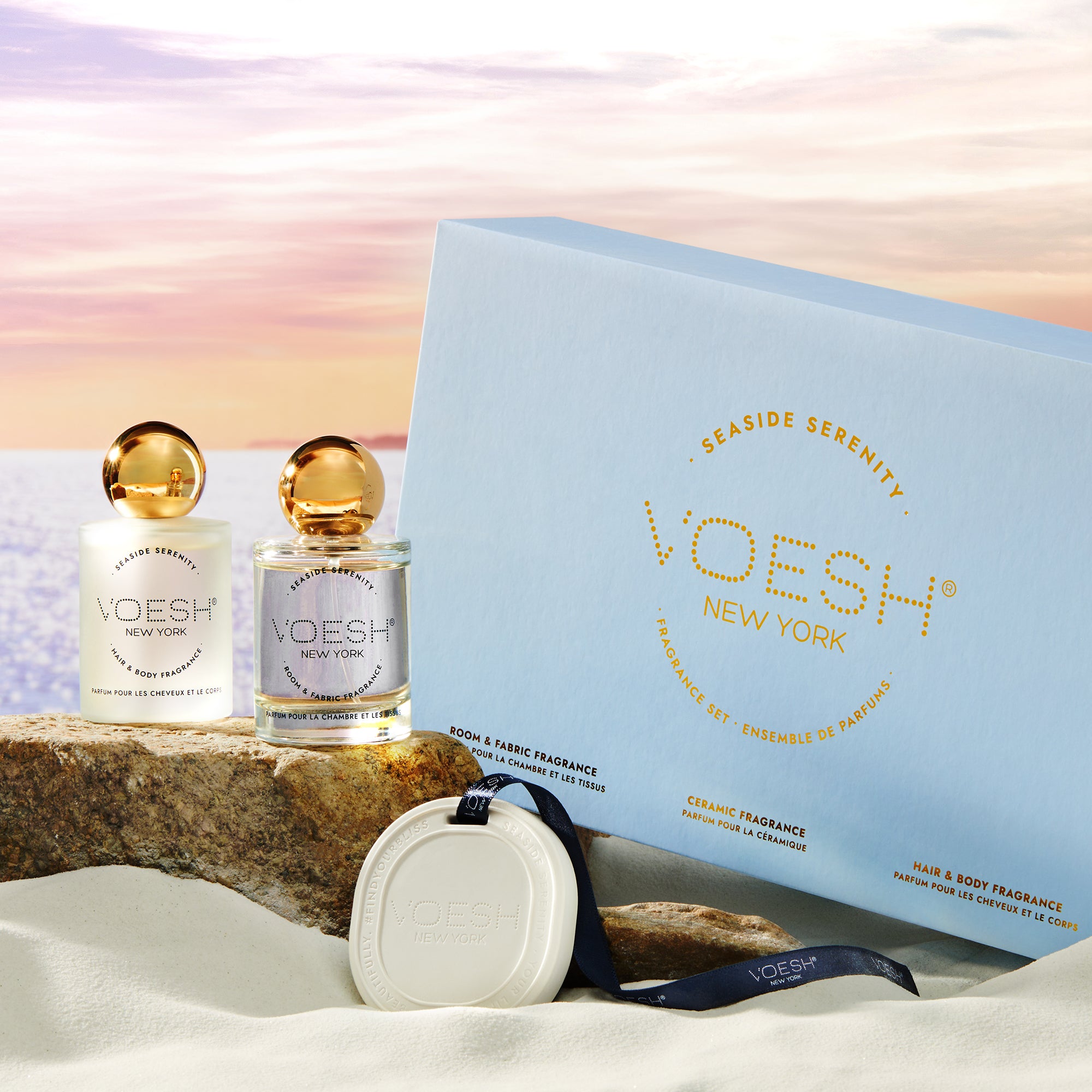 Seaside Serenity Fragrance Set Box, Ceramic Fragrance, Hair & Body Fragrance, and Room & Fabric Fragrance on a beach background.